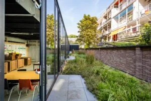 Moderne gemeenschappelijke ruimte aan de Karel du Jardinstraat met glazen gevel en uitzicht op een groene binnentuin naast een woongebouw.